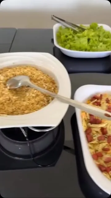 Travessa de farofa com colher, salada de alface e macarrão com calabresa no balcão