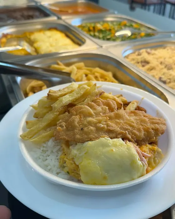 Marmita com filé de frango empanado, batata frita, arroz e frango gratinado, em frente às cubas do balcão